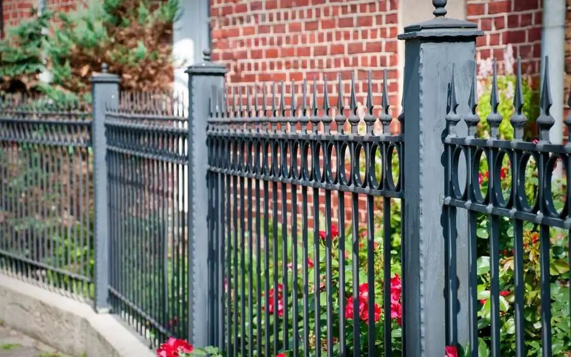 Black ornamental iron fence and metal posts in front of a brick building