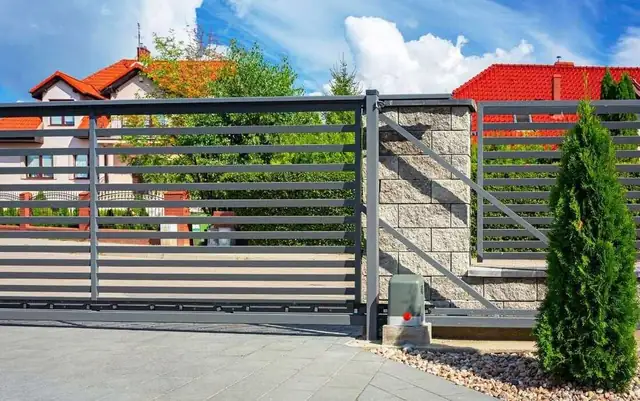 Gray horizontal slat sliding gate with an opener mounted on a stone pillar