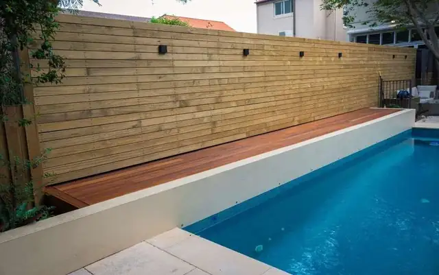 Tall horizontal wood privacy fence along one side of a lap pool