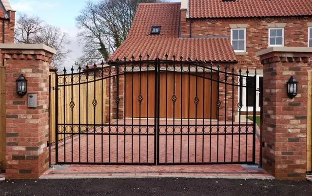 Black ornamental iron driveway gate between brick pillars