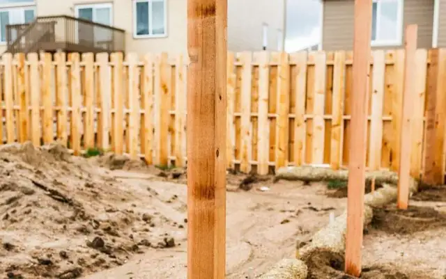 New wood fence posts set in the ground in front of a partly built wood fence