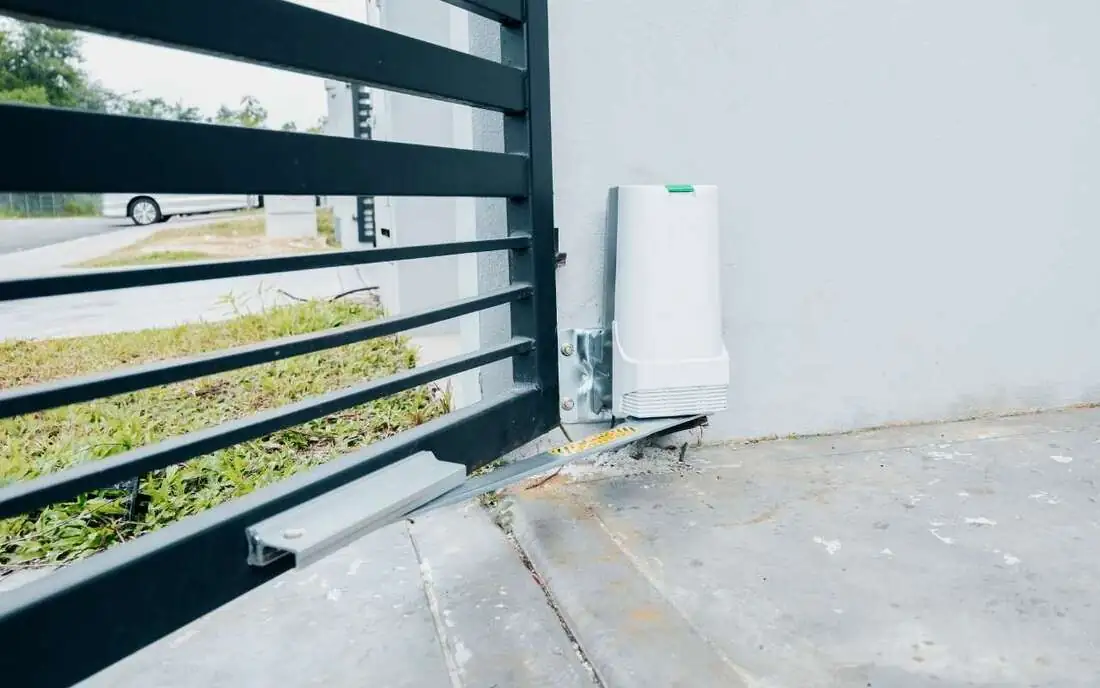 Automatic opener motor at the base of a black horizontal sliding gate