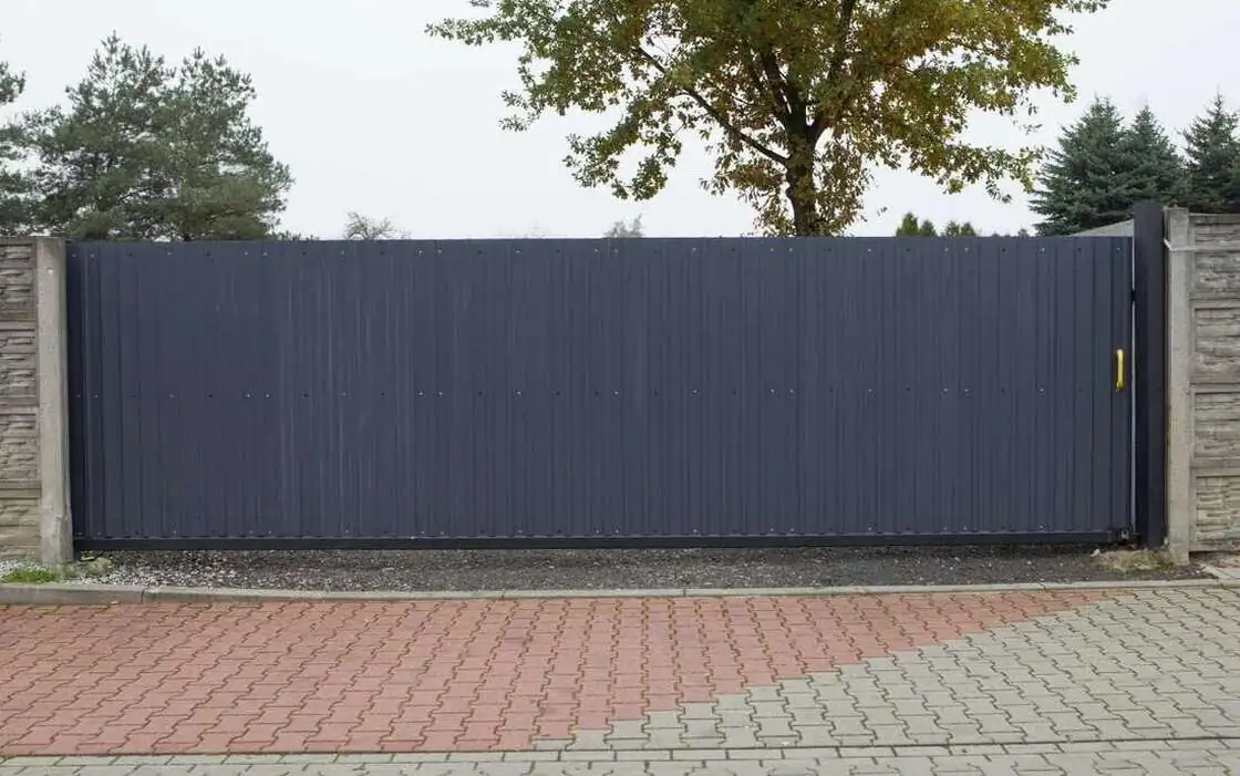 Dark gray solid sliding gate across a paved driveway entrance