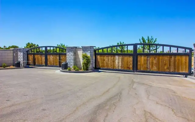Two arched driveway gates with wood panels set in black metal frames at a gated entrance