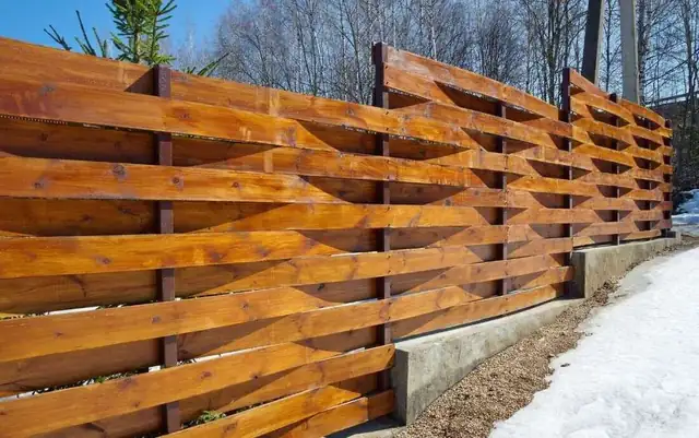 Woven horizontal wood fence on a concrete curb with snow on the ground